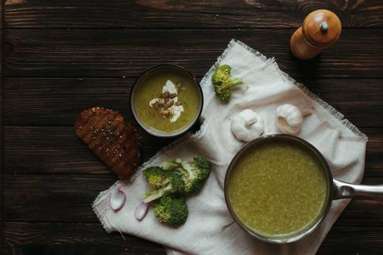 Top view of saucepan with broccoli puree soup on white napkin with garlic and toasted bread slice
