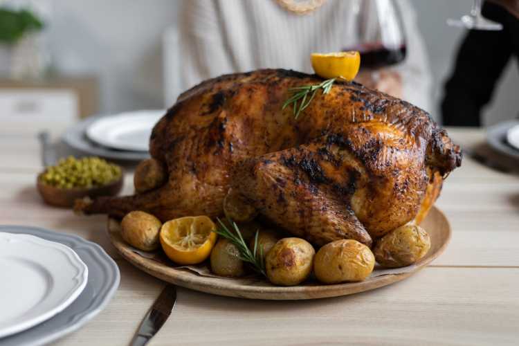 From above of big turkey roasted with lemon and potatoes on round wooden tray placed on table for celebrating Thanksgiving Day