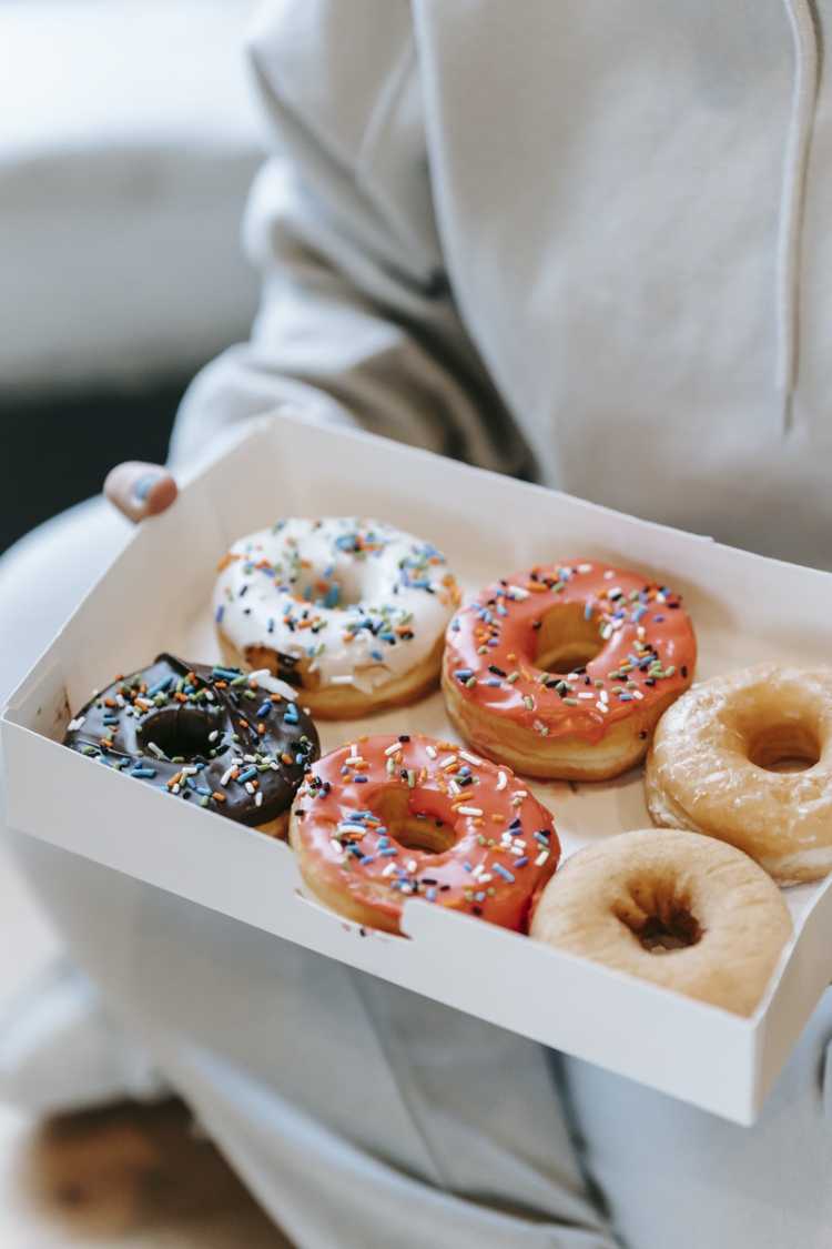 Crop unrecognizable person demonstrating box with delicious doughnuts