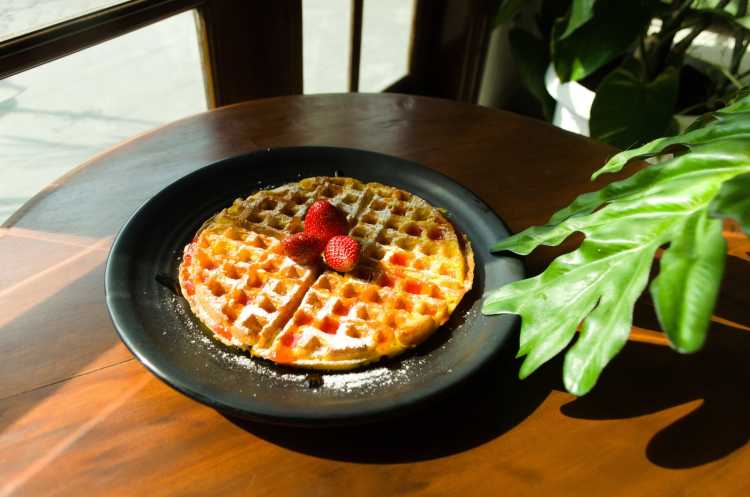 waffle with strawberry and green leaf on black ceramic plate